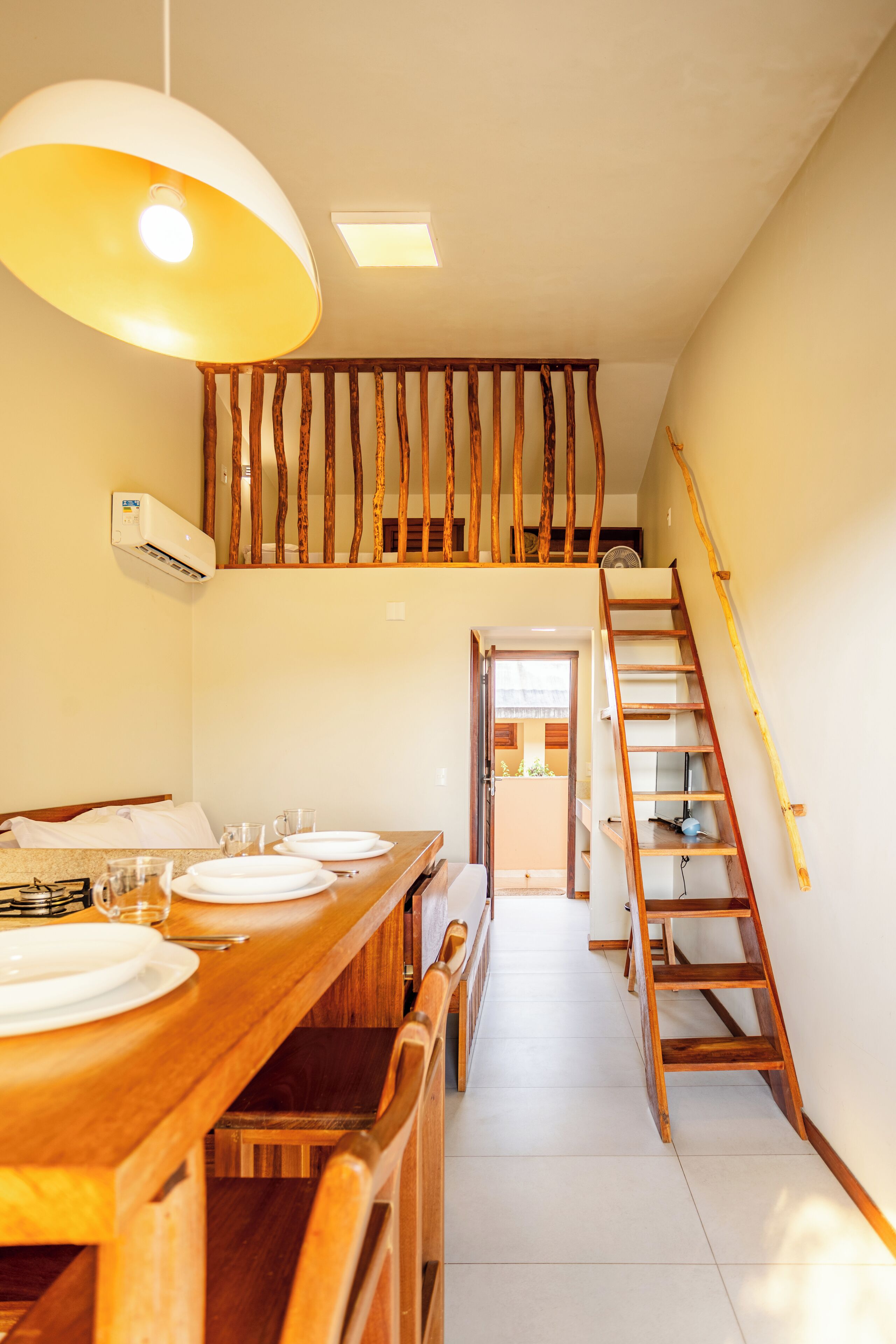 Un coin repas avec une table en bois dressée pour quatre personnes, un escalier avec une rampe en bois et un luminaire au plafond.