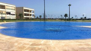 Una amplia piscina al aire libre con superficie de agua azul cristalina, rodeada por una zona pavimentada.