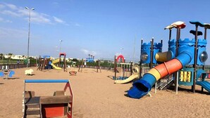 Un parque infantil arenoso con un tobogán azul, uno rojo y amarillo, y diversas estructuras de juego.