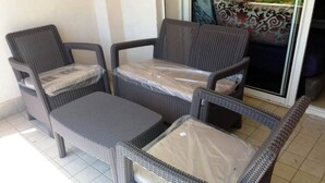 Juego de mobiliario de mimbre con cubiertas de plástico, que incluye una silla, un sofá y una mesita, ubicado cerca de un vidrio.