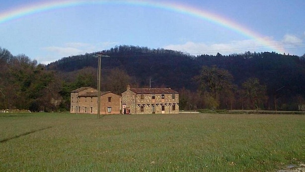 Un edificio in pietra su due piani con tetto piatto, circondato da un prato erboso e una collina boscosa sullo sfondo.
