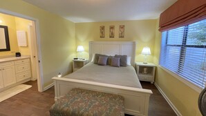 A bedroom with a bed, bedside tables, a bench, a window with blinds, and artwork on the wall. - Desirable Ground Floor Condo in a Gated Community with Pool & Fitness Center! (Saint Simons Island)