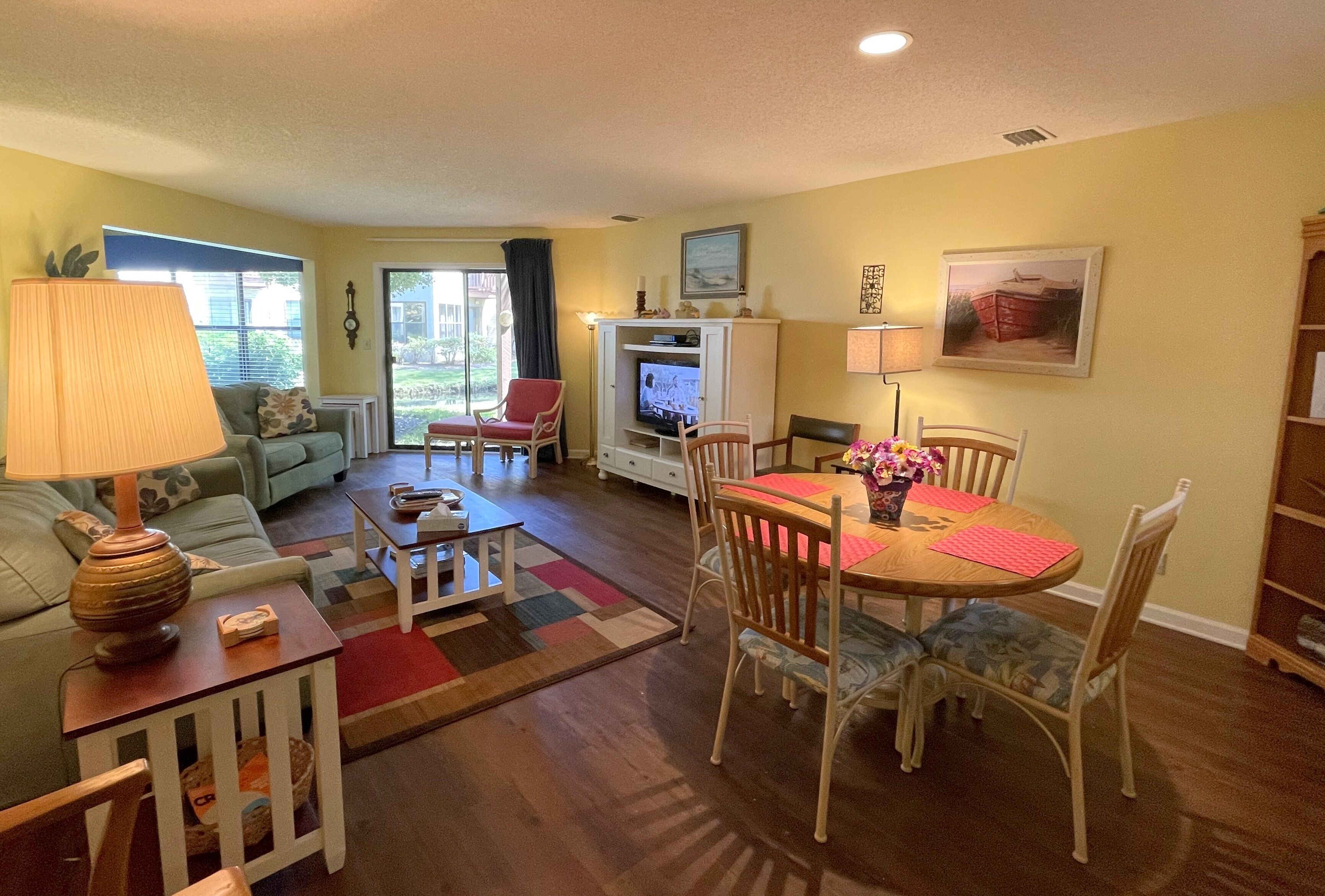 A living room with a sofa, a coffee table, a dining table with chairs, a TV, and a bookshelf.