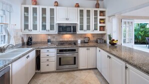 A kitchen with white cabinets, a granite countertop, a microwave, an oven, and a sink. - Beachfront Bliss with Plunge Pool - Seashells (Paynes Bay)