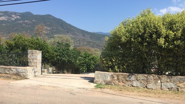 Eine gepflasterte Straße führt zu einem Steintor, vor dem sich ein Berg erstreckt.
