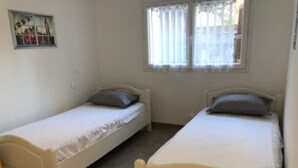 Zwei Einzelbetten mit weißer Bettwäsche und grauen Kissen in einem Zimmer mit Fenster und einem Bild an der Wand.