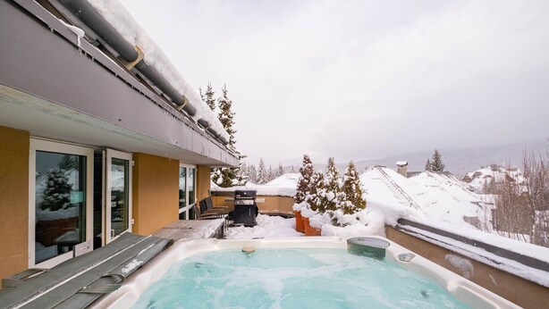 Un jacuzzi con vistas a montañas nevadas y una parrilla de barbacoa al aire libre.