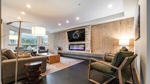 Una sala de estar moderna con chimenea, asientos cómodos y un televisor grande montado en una pared de piedra.