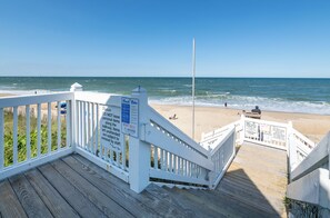 A wooden deck with a railing overlooking a beach. There are signs with beach rules and a lifeguard stand.