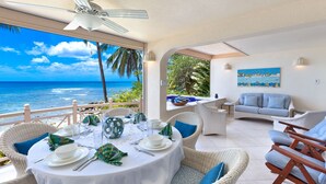 A dining area with a view of the ocean, wicker furniture, and a painting on the wall. - Beachfront Condo with Plunge Pool - Reeds House 10 (Reeds Bay)