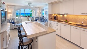 A modern kitchen with a central island, white cabinetry, and a view of the ocean. - Beachfront Condo with Plunge Pool - Reeds House 10 (Reeds Bay)