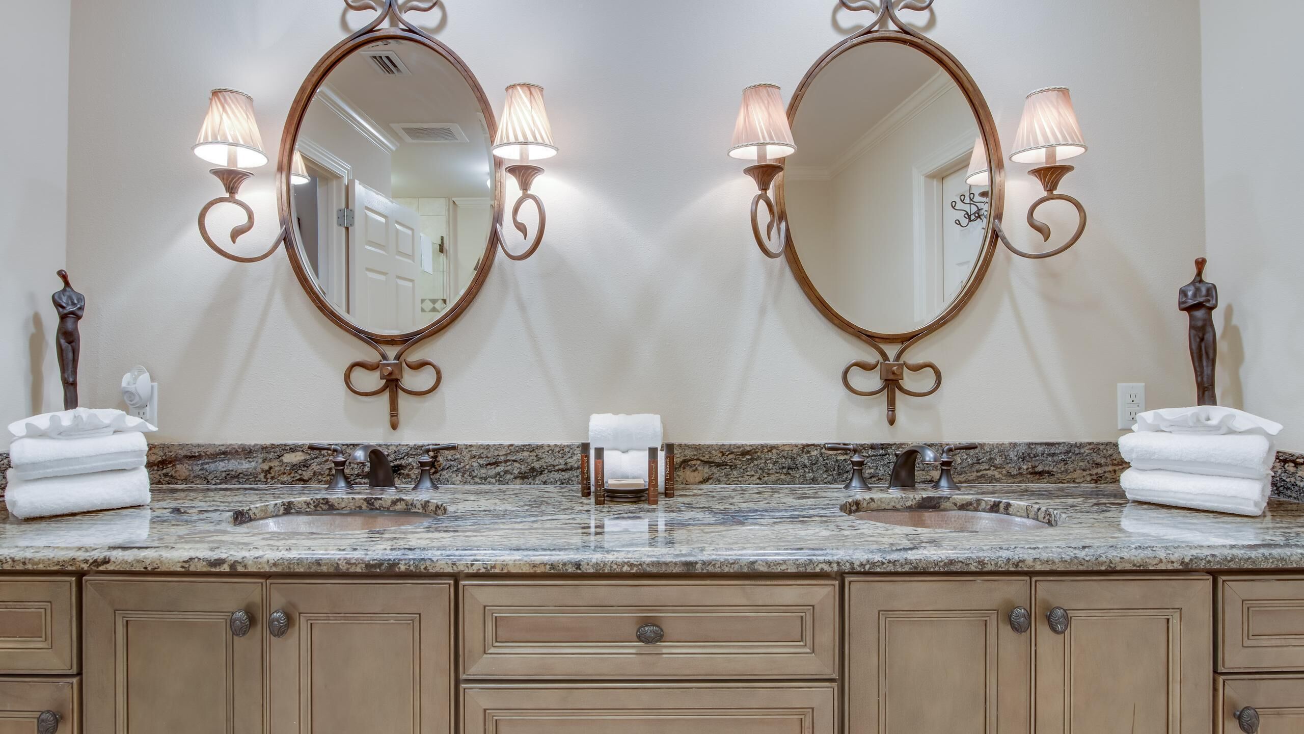 Baño con dos lavamanos, encimeras de mármol, muebles de madera y espejos con apliques.