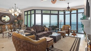 A spacious living room with a large window, a ceiling fan, and a view of the ocean. - Breathtaking Gulf Views – Welcome to Phoenix West 1103! (Orange Beach)