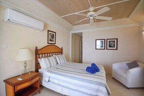 A hotel room with a bed, a bedside table with a lamp, a ceiling fan, and a white sofa. - Beachfront 2-Bed Condo with Plunge Pool - Indramer 1 (Worthing)