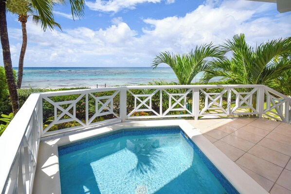 A swimming pool with a white deck and railing, surrounded by tropical plants and overlooking a beach. - Beachfront 2-Bed Condo with Plunge Pool - Indramer 1 (Worthing)