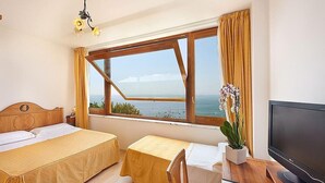 Une chambre d’hôtel avec deux lits, un bureau avec une chaise, une télévision et une fenêtre donnant sur la mer.