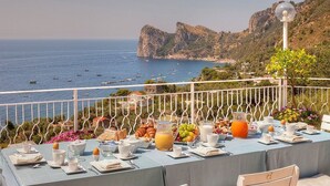 Une table à manger dressée avec des aliments pour le petit-déjeuner, offrant une vue sur la mer et les falaises rocheuses.