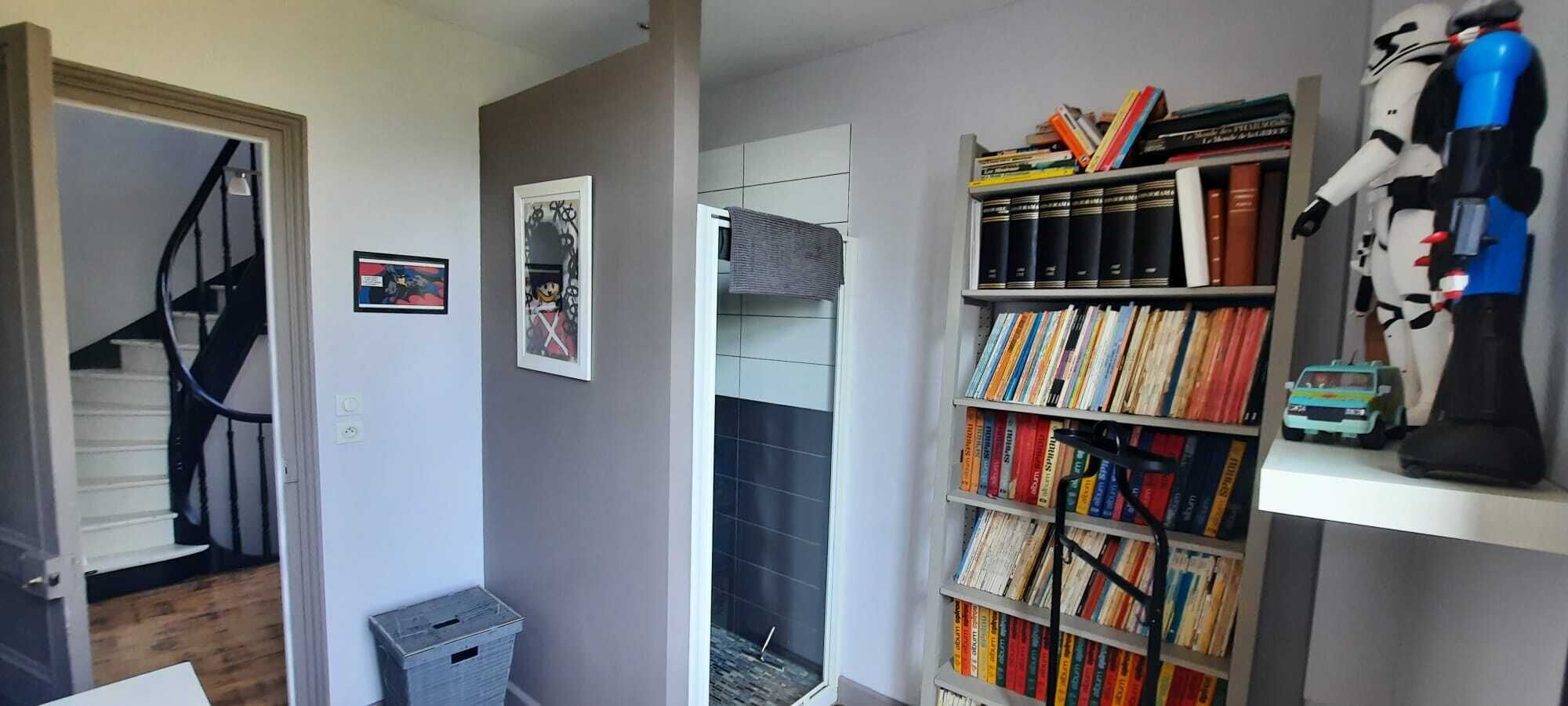 A room with a bookshelf filled with books, a toy car, and a Star Wars helmet.