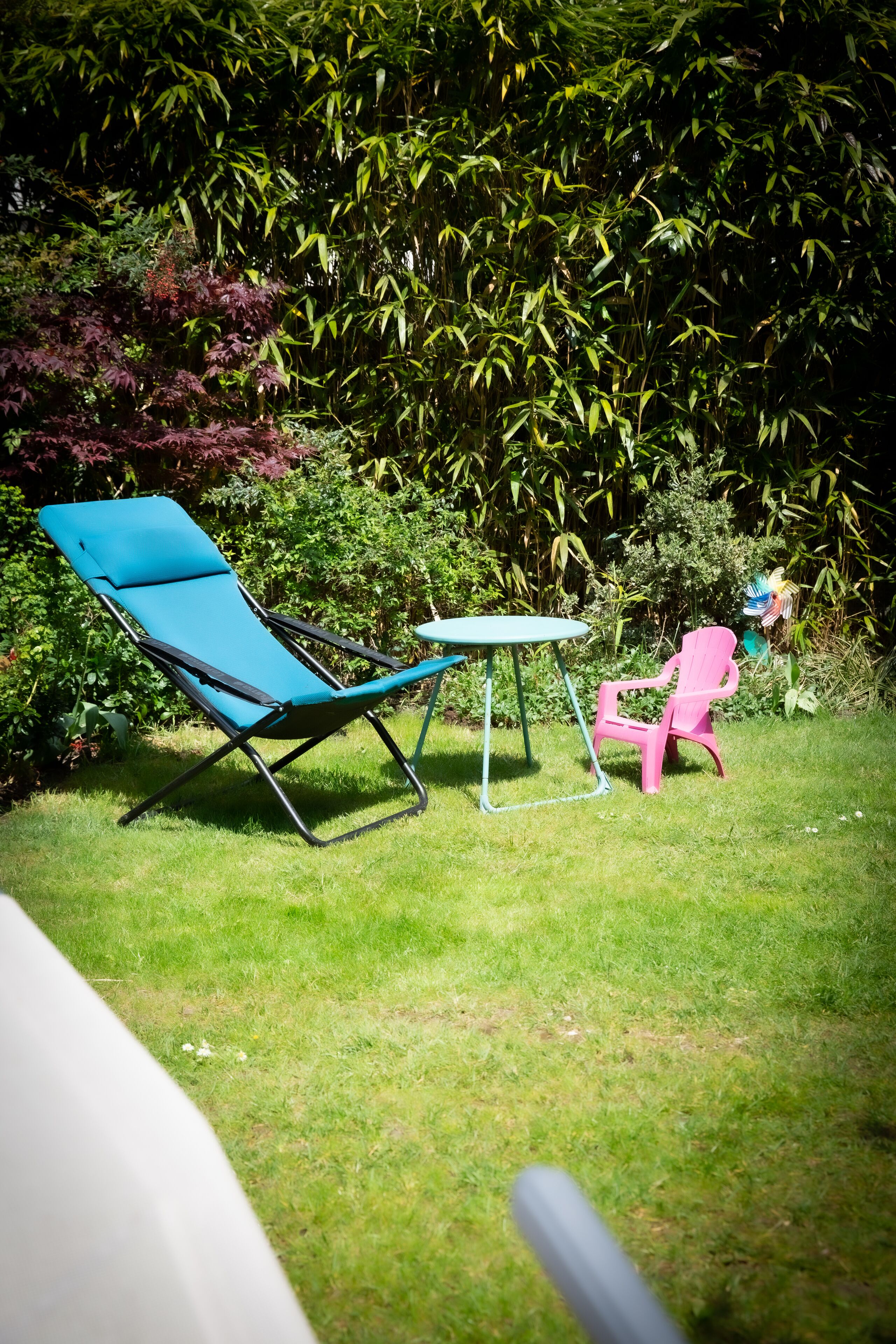 Un jardín con una silla de jardín azul, una mesita pequeña y una silla rosa.