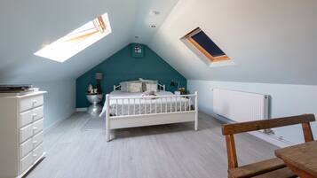 Quarto com teto inclinado, cama, cômoda e janela.
