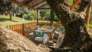 Un patio exterior con una mesa y sillas de madera, rodeado por una valla de madera, situado en un jardín exuberante.