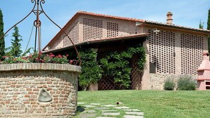 Una casa de ladrillo con techo de tejas, un muro de piedra con un detalle decorativo, y un jardín con un sendero de piedra.