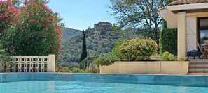 A swimming pool with a view of a castle on a hill, surrounded by lush greenery and flowering plants. - AT THE CHATEAU D'O LE CHATELET (Corbère)