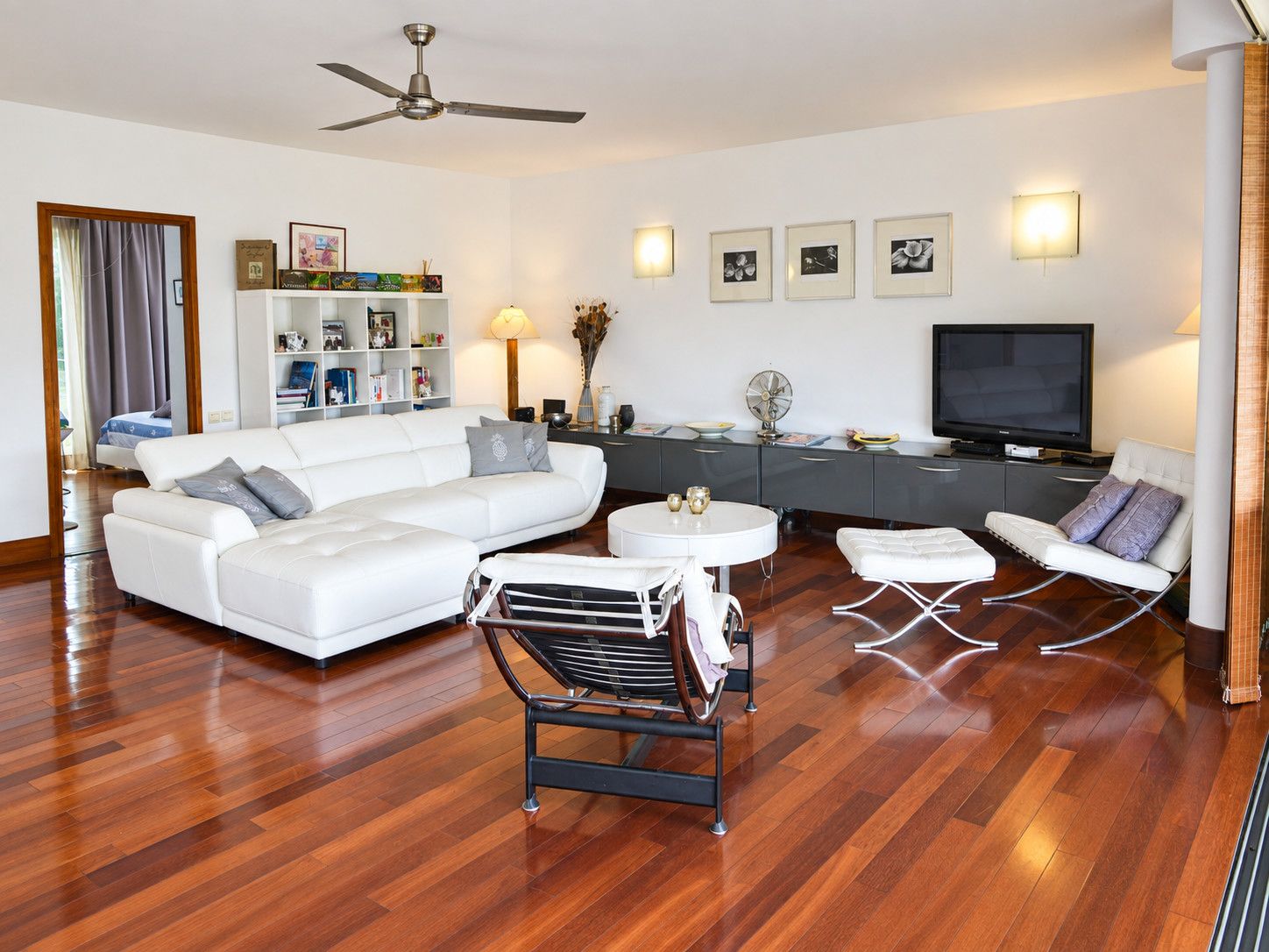 Un salon moderne avec un canapé blanc, un fauteuil noir, une petite table ronde, un téléviseur à écran plat et un ventilateur de plafond.
