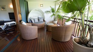 Une terrasse en bois agrémentée de meubles en osier, notamment un coin salon circulaire avec des coussins, une petite table et une plante en pot.