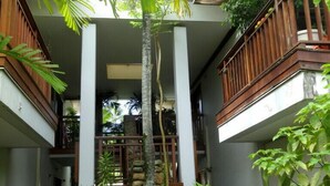 Un immeuble à plusieurs étages, doté d’un escalier central entouré d’une végétation luxuriante et de plantes tropicales.