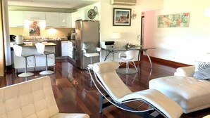 Un salon moderne comprenant un canapé, un fauteuil inclinable, un coin repas avec une table et des chaises, et une cuisine en arrière-plan.