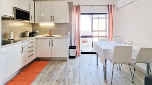 A compact kitchen with modern appliances, a dining area with a table and chairs, and a view through a glass door to an outdoor space.