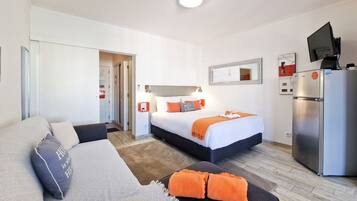 A hotel room with a bed, a sofa, a TV, and a refrigerator.