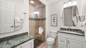 Et badeværelse med brusebad, toilet, vaskebord og et billede i ramme på væggen.