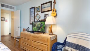 Un salon avec un meuble de rangement en bois pour les appareils multimédias, une télévision, une guitare et un fauteuil bleu.