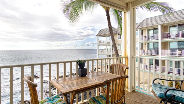 Une table et des chaises en bois sur un balcon, avec vue sur l’océan et sur un immeuble doté de balcons.