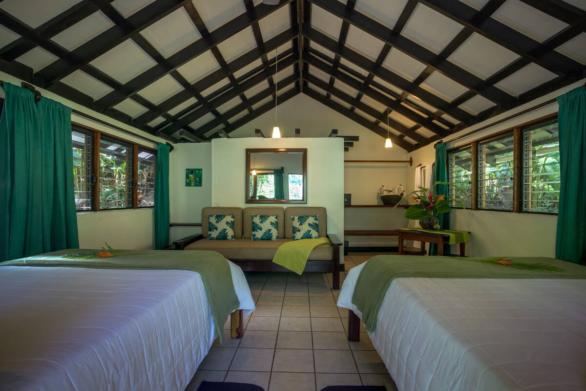 Una habitación con dos camas, un sofá, una mesita y un espejo.