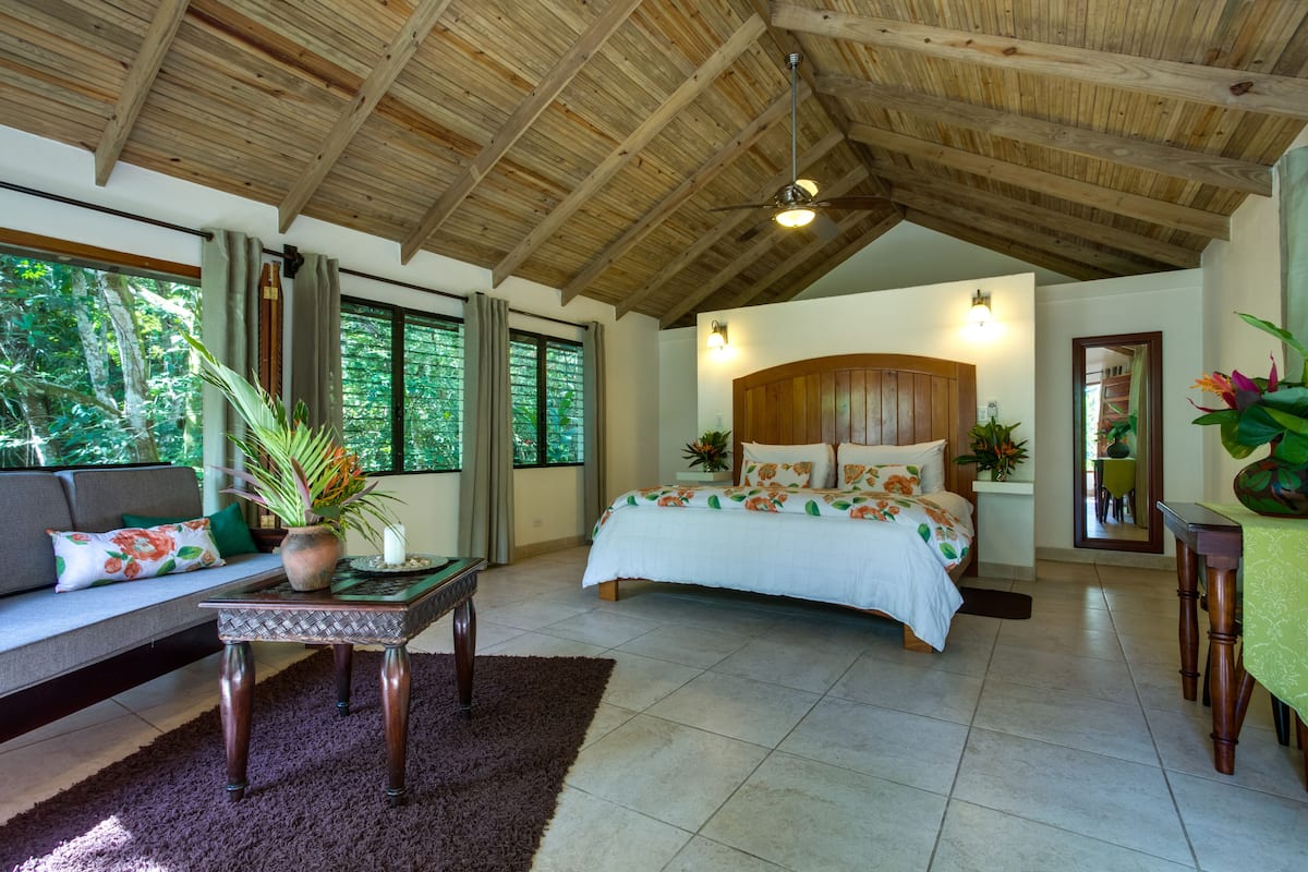 Un dormitorio espacioso con una cama grande, techo de madera y vistas al exterior.