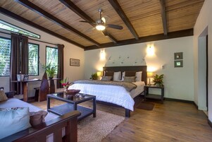 Ein geräumiges Schlafzimmer mit einem großen Bett, einem Deckenventilator und Blick ins Freie durch die Fenster.