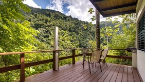Un terrazzo in legno con tavolo e sedie, affacciato su una rigogliosa foresta verde e montagne.
