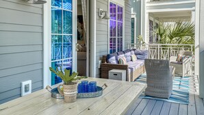 A covered porch with wicker furniture, a table with blue glass tumblers, and a potted plant.