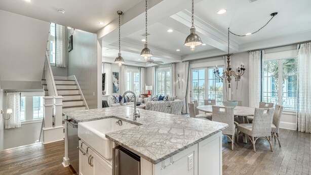 A spacious kitchen with a large island, white cabinetry, and a dining area with wicker chairs.