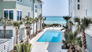 A pool area with a view of the ocean, surrounded by palm trees and a fence.