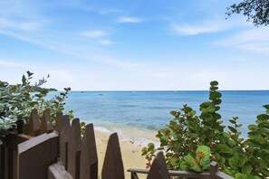 A beach view with a wooden fence, greenery, and calm sea.