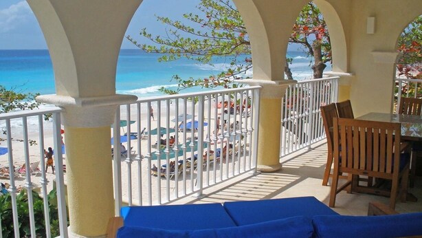 Een balkon met uitzicht op het strand en de oceaan, met een tafel, stoelen en een zithoek met kussens.