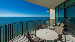 Un balcón con una mesa redonda y cuatro sillas, con vista a un mar azul y despejado.