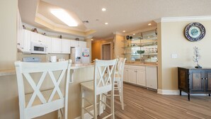 Una cocina con armarios blancos, suelo de madera y una zona de bar con sillas blancas.