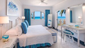A bedroom with a bed, a desk, and a chair, a large window with a view of the beach, and a ceiling fan. - Private Beachfront Oasis - Reeds House 1 (3 bed) (Reeds Bay)