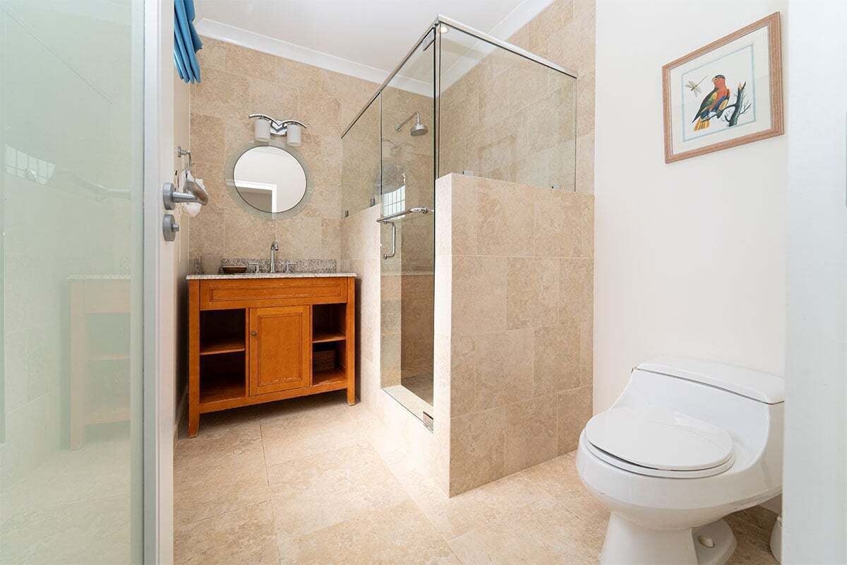 A modern bathroom with a glass shower enclosure, a wooden vanity, a round mirror, and a white toilet.