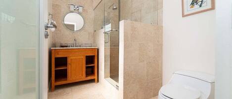A modern bathroom with a glass shower enclosure, a wooden vanity, a round mirror, and a white toilet.